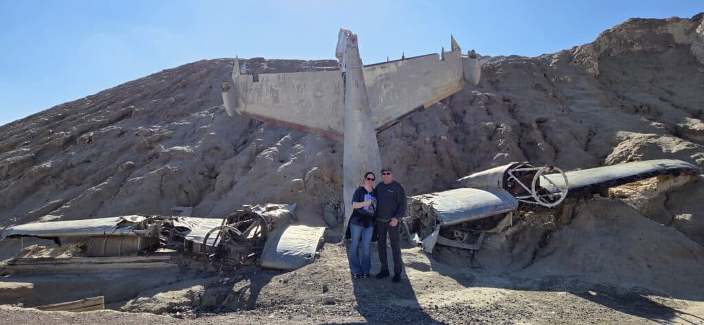 Couple poses by a weathered plane wreck on a Nevada hillside, perfect for Las Vegas ATV tours or Ghost Town sightseeing.