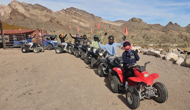 Helmeted riders on ATVs line up for a Nevada desert tour near Las Vegas, with mountains and rugged terrain in the background.