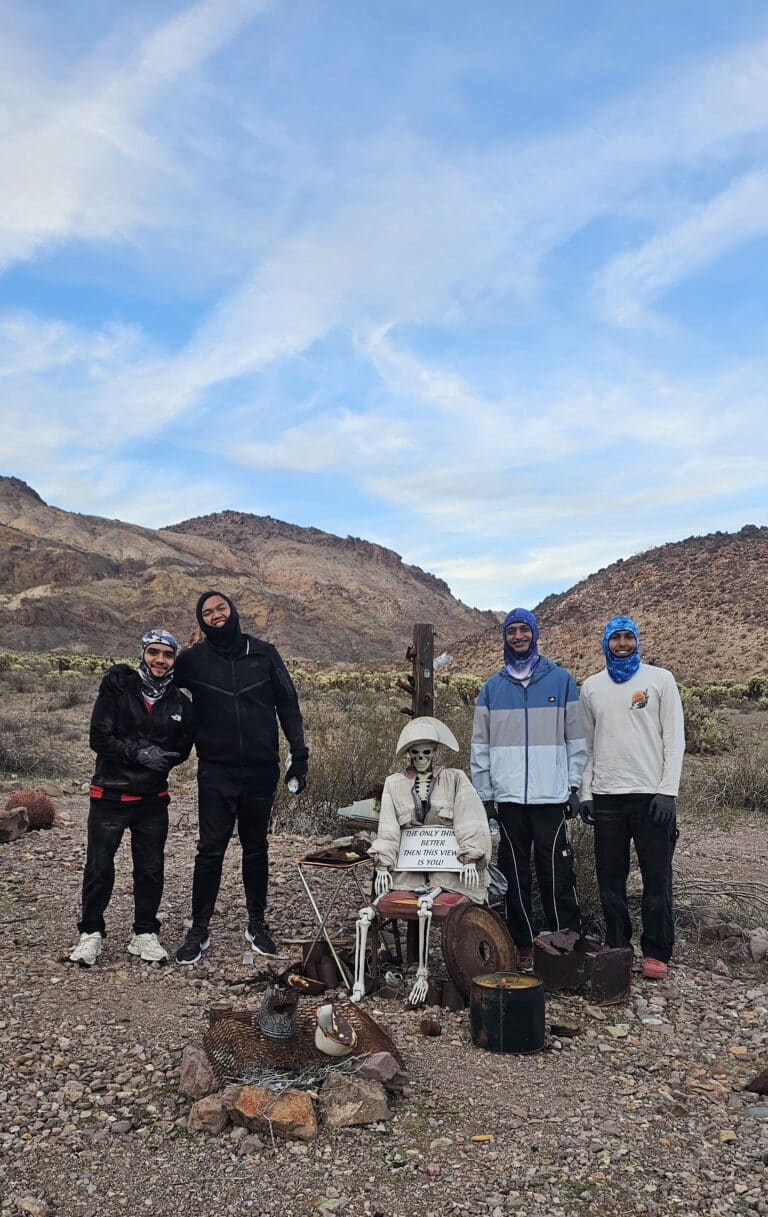 Group posing with skeleton at table in Nevada desert near Las Vegas, mountains behind; perfect for Ghost Town sightseeing adventures.