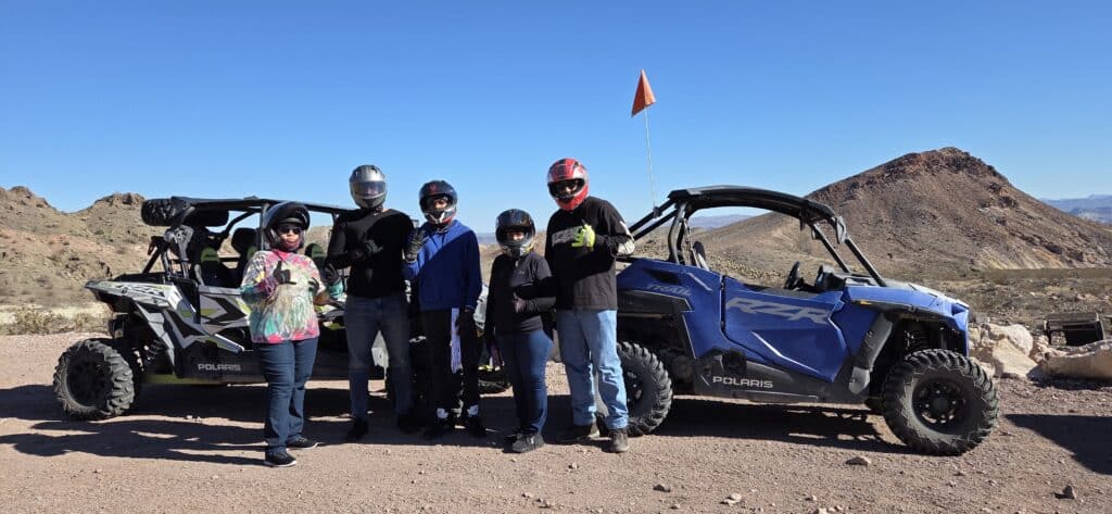 Group in riding gear poses by blue Polaris ATVs on a Nevada desert trail near Las Vegas, ideal for RZR off-road tours.
