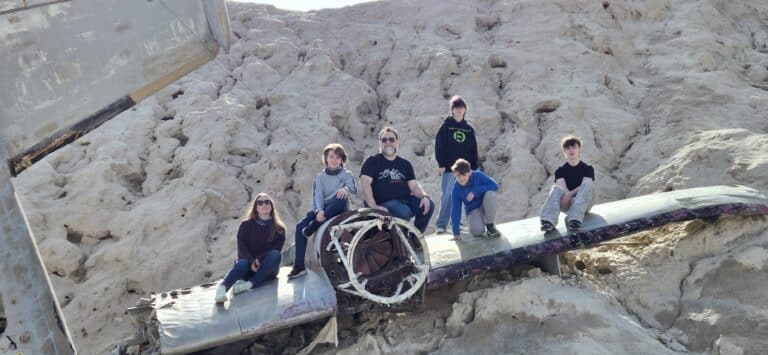 Group of adults and kids sit on a crashed plane wreck in Nevada desert near Las Vegas, perfect for Ghost Town sightseeing tours.