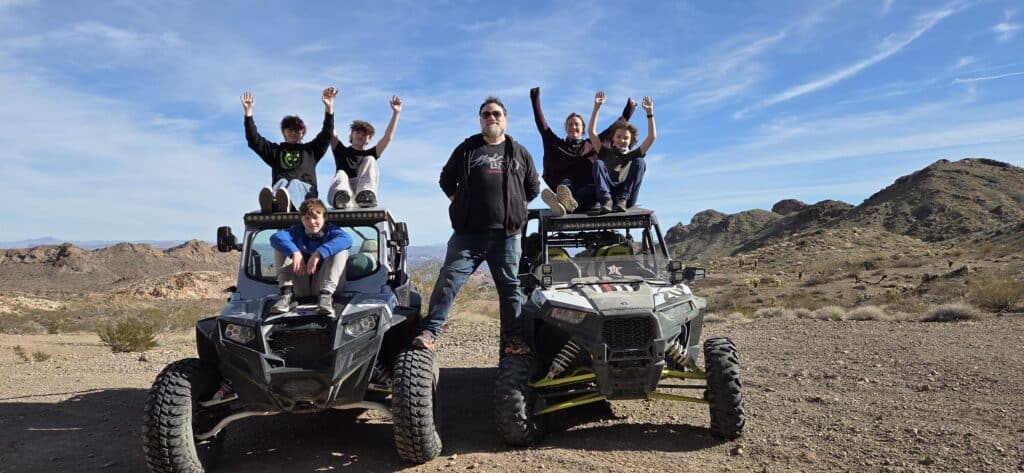 Family enjoying an ATV tour near Las Vegas in the Nevada desert, kids cheering on off-road vehicles with rocky hills and blue sky.