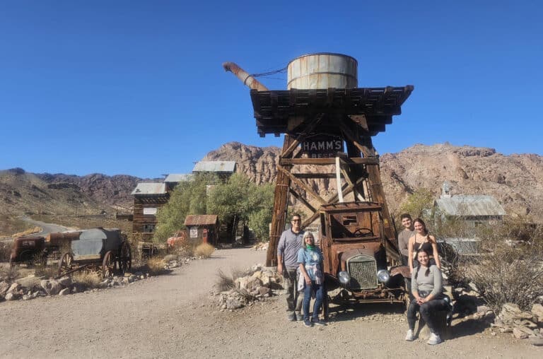 Five friends pose by a rusty truck and HAMMS BEER water tower in a Nevada ghost town near Las Vegas, perfect for ATV tours.