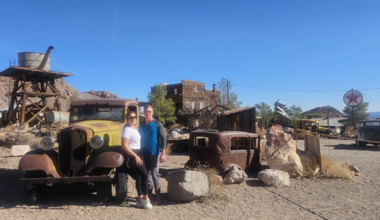 Smiling friends by a rusty car in a Nevada ghost town near Las Vegas, perfect for ATV tours and Ghost Town sightseeing.