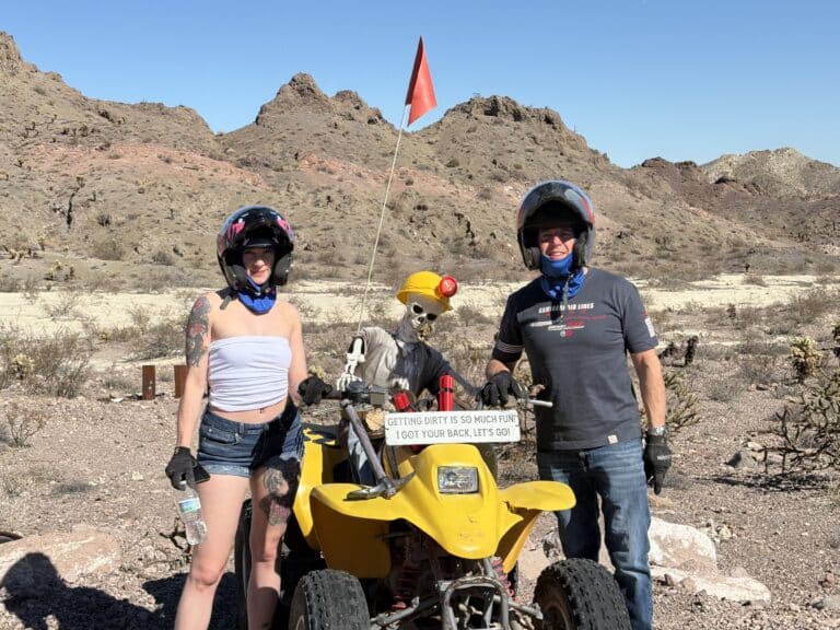 ATV tour near Las Vegas: two helmeted riders and a gear-clad skeleton pose by their ride in the Nevada desert.