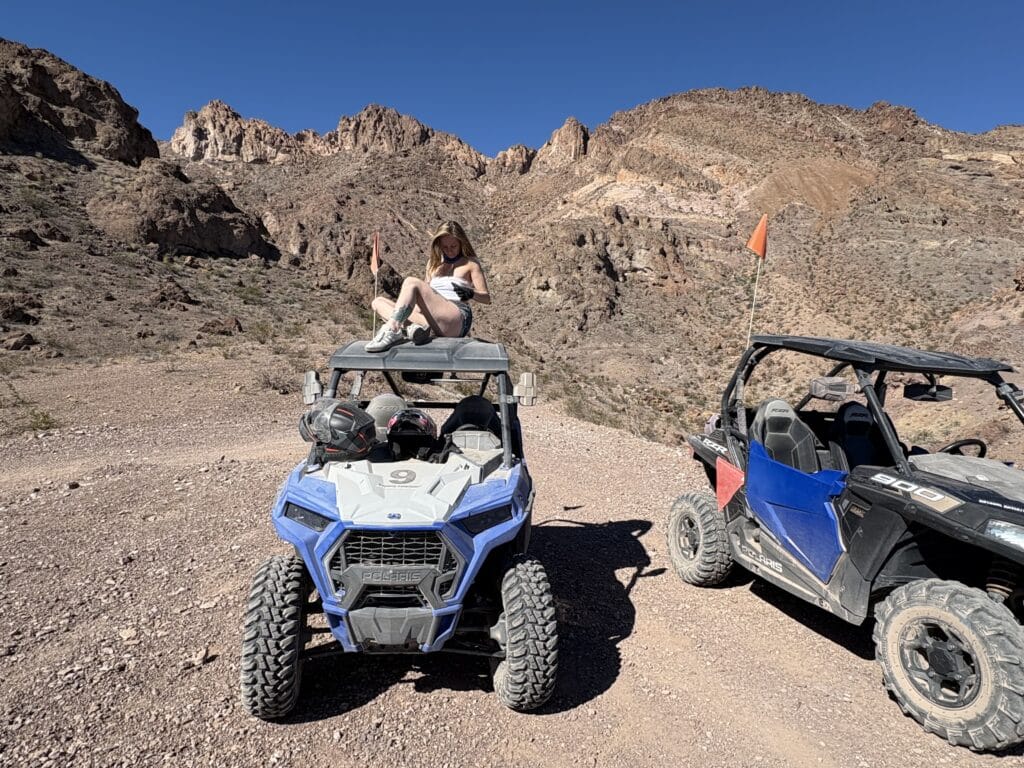 Explorer atop blue RZR in Nevada desert near Las Vegas, with ATV tour group and Colorado River mountains in the background.