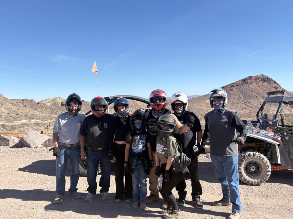Adventure group in helmets by an off-road vehicle during a Las Vegas Nevada RZR ATV tour in the rocky desert near the Colorado River.