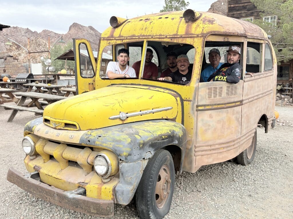 Six men relax in a vintage yellow bus at a Nevada ghost town, smiling after ATV tours near the Colorado River and Las Vegas.