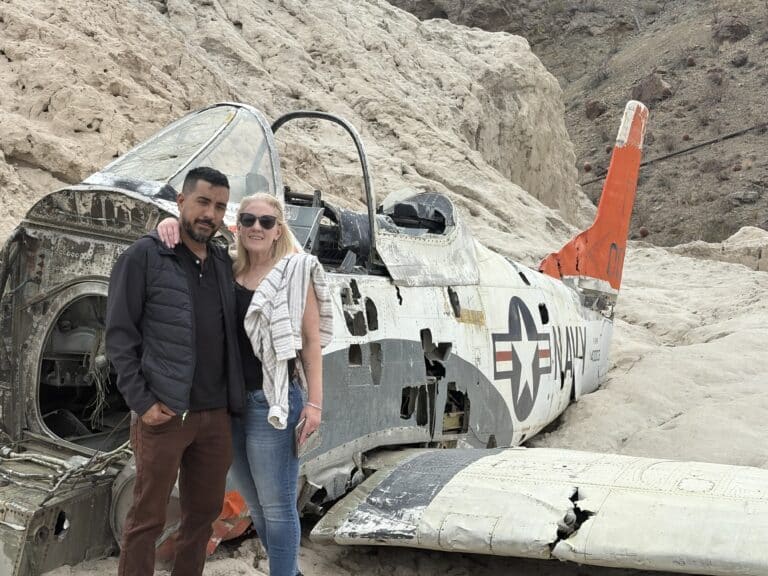 A couple stands arm-in-arm by a weathered aircraft wreck in Nevada's rocky terrain, perfect for Las Vegas ATV tours.