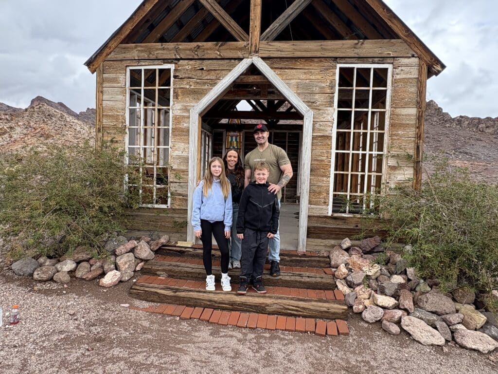 Smiling family of four on rustic steps near Las Vegas, Nevada, perfect for Ghost Town sightseeing in the desert landscape.