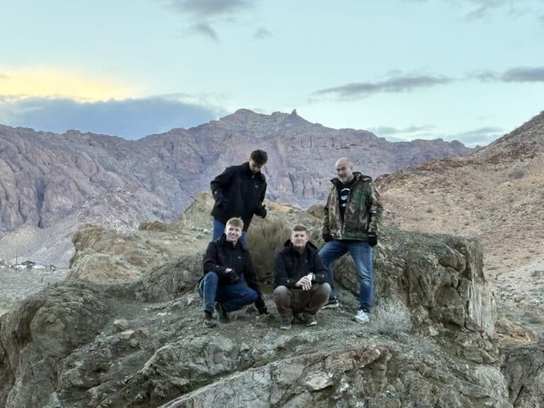 Four people in jackets enjoy a desert mountain view near Las Vegas, Nevada, with rugged hills and cloudy dusk skies—perfect for ATV tours.