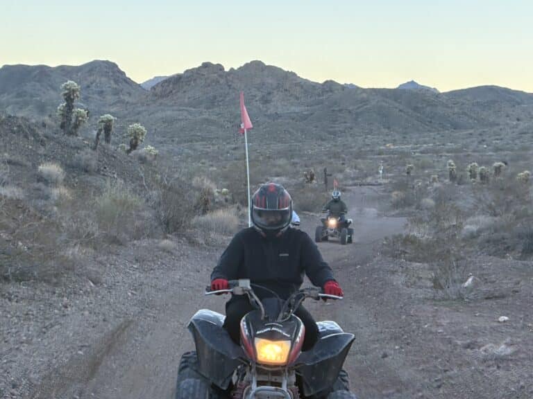 Two people enjoy an ATV tour near Las Vegas, riding dirt trails past cacti and mountains in the Nevada desert.