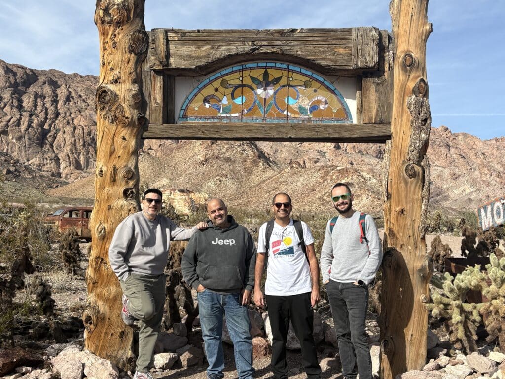 Four men smile under a rustic stained glass arch in Nevada desert near Las Vegas, with cacti and rocky hills—perfect for ATV tours.