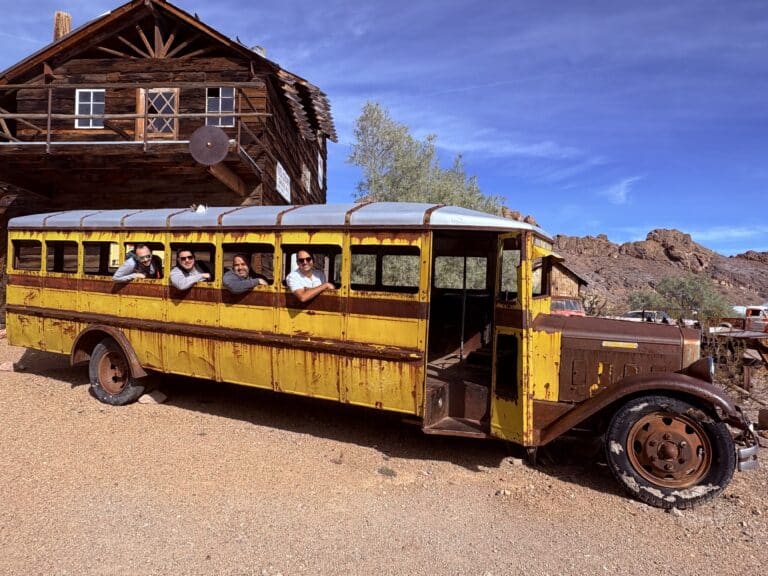 Smiling friends lean from a rusty yellow school bus near a Nevada ghost town, perfect for ATV tours or Colorado River sightseeing.