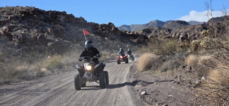 ATV riders explore a dusty desert trail near Las Vegas, Nevada, with rocky hills and blue sky—perfect for thrilling RZR tours.