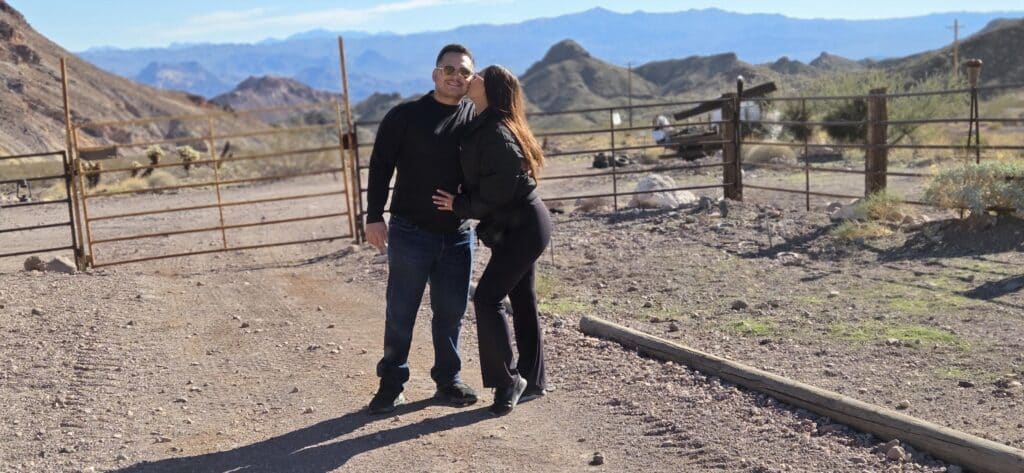 A smiling couple in black stands on a dirt road near Nevada’s rugged hills, perfect for ATV tours by Las Vegas and the Colorado River.