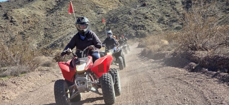 Adventure seekers on red ATVs ride a dusty Nevada trail near Las Vegas, enjoying scenic hills on an exciting ATV tour.