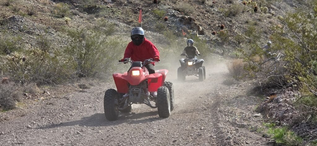 ATV riders explore a dusty Nevada desert trail near Las Vegas, with rocky terrain and shrubs, on an exciting off-road tour.