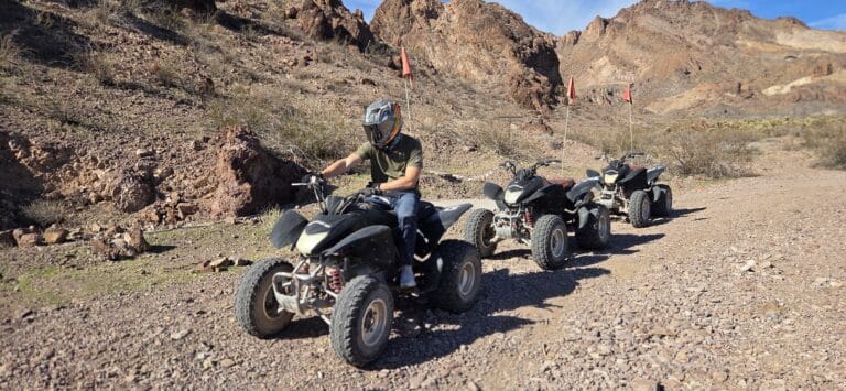 Rider on ATV leads a group on a rocky Nevada desert trail near Las Vegas, with brown mountains—perfect for ATV tours.