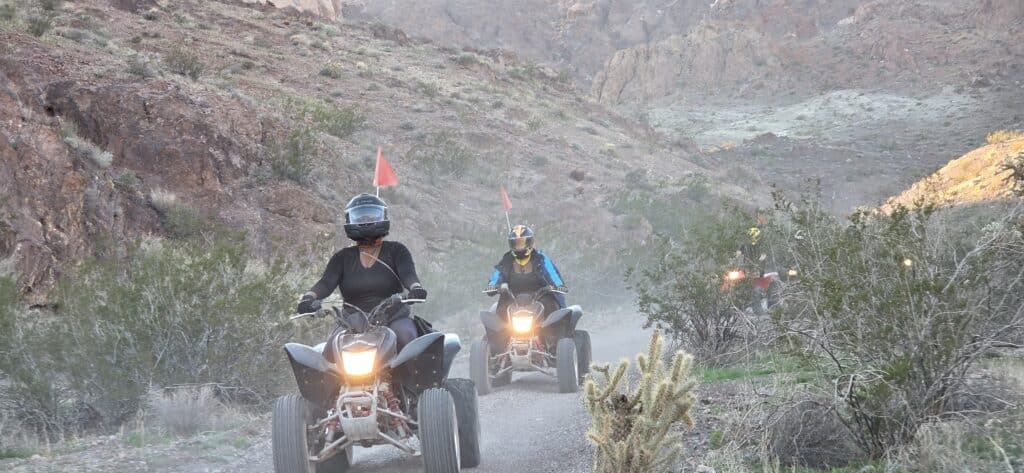 ATV riders in helmets explore a rocky Nevada desert trail near Las Vegas, cacti dotting the path, with more on an ATV tour behind.