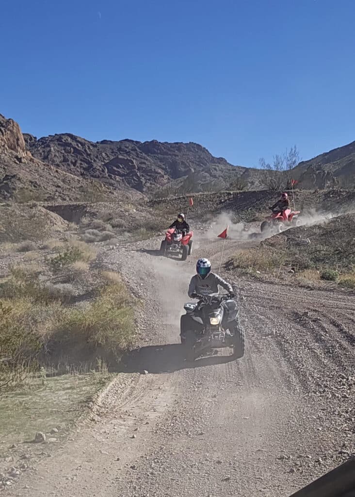 ATV riders on a dusty Nevada trail near Las Vegas, mountains behind, red flags flying—perfect for off-road RZR adventure tours.