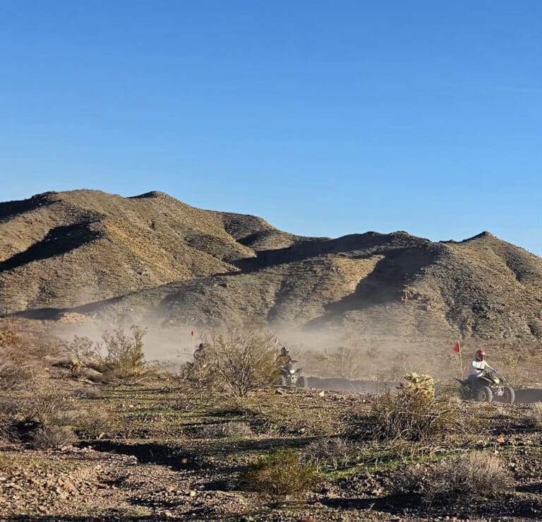 ATV tour in Nevada: four riders explore a dusty desert trail near Las Vegas with sunlit hills and rugged scenery in the background.