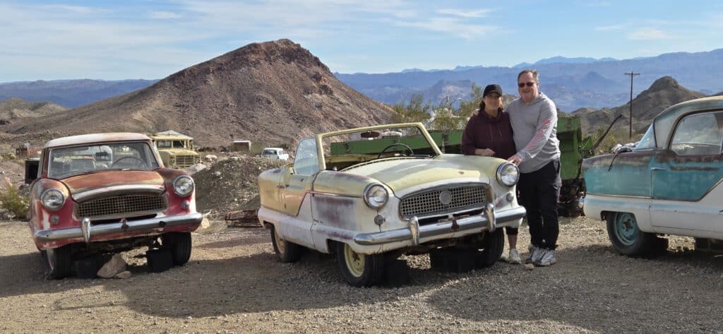 Two people by a vintage yellow convertible near Nevada’s rocky hills, perfect for Las Vegas Ghost Town sightseeing adventures.