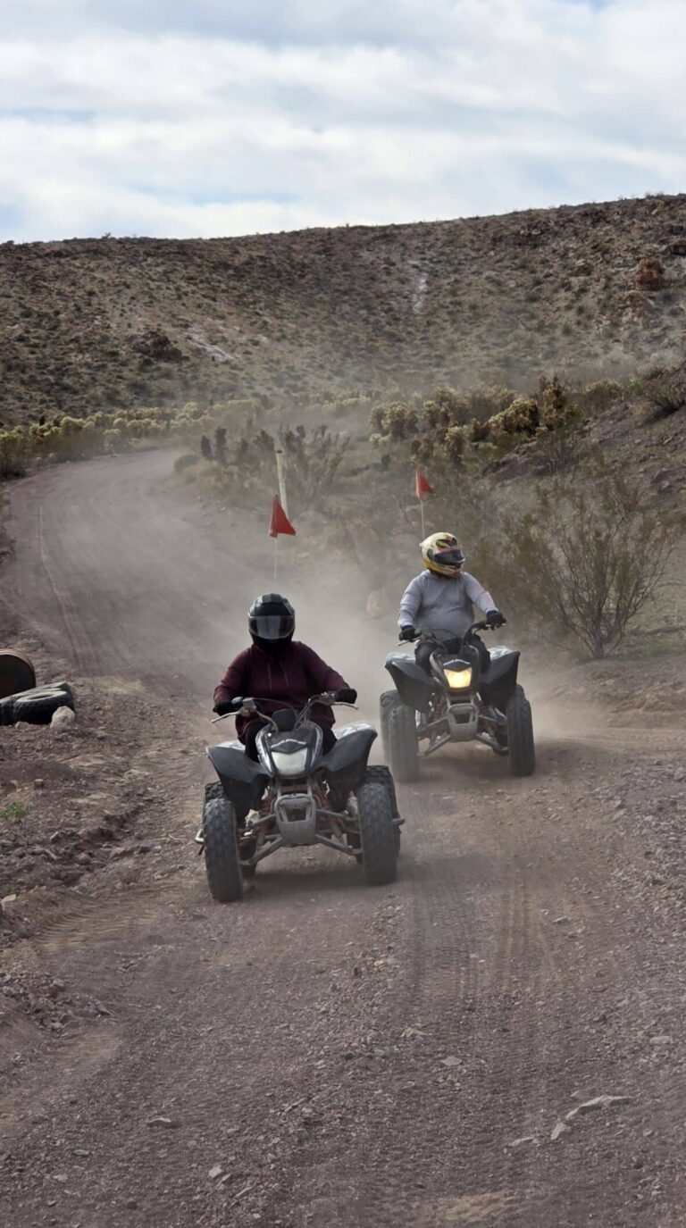 ATV riders explore a dusty Nevada desert trail near Las Vegas with hills, bushes, and clouded skies on an exciting ATV tour.