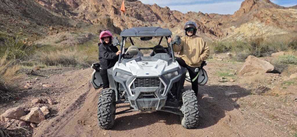 Helmeted adventurers stand by a white ATV on a rocky Nevada desert trail near Las Vegas, ready for an off-road RZR tour.