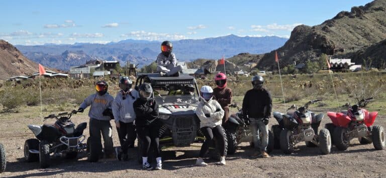 Group with helmets and gear poses by ATVs and RZR in Nevada desert near Las Vegas, ready for ATV tours and off-road adventure.