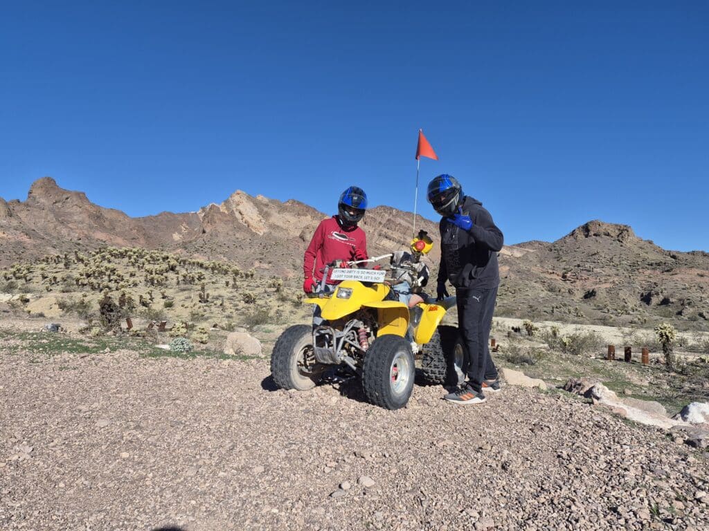 Adventurers in helmets pose by a yellow ATV on Nevada desert terrain near Las Vegas, ideal for ATV tours and RZR off-road rides.