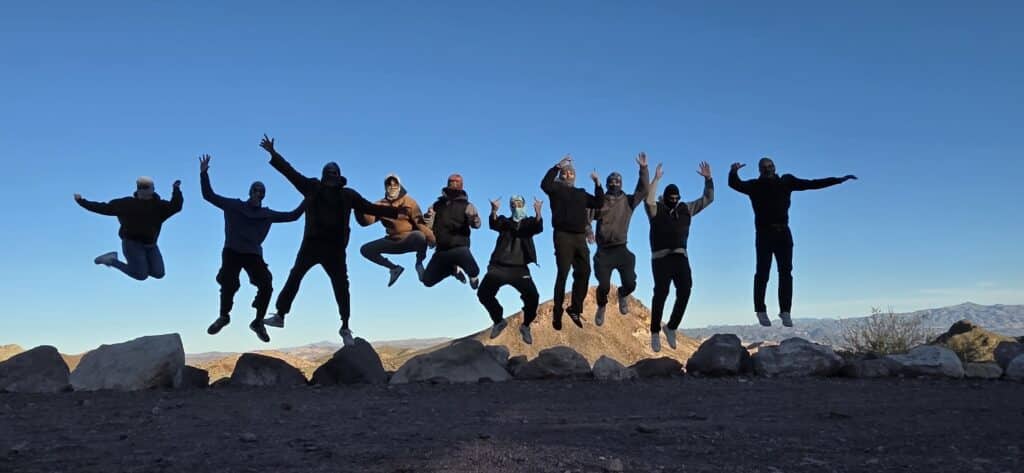 Nine people jump in sync above Nevada desert hills, celebrating a Las Vegas ATV tour near the Colorado River.
