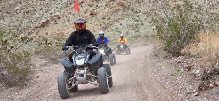 ATV riders cruise a dusty Nevada desert trail near Las Vegas, leading an ATV tour past rocky hills and desert shrubs.