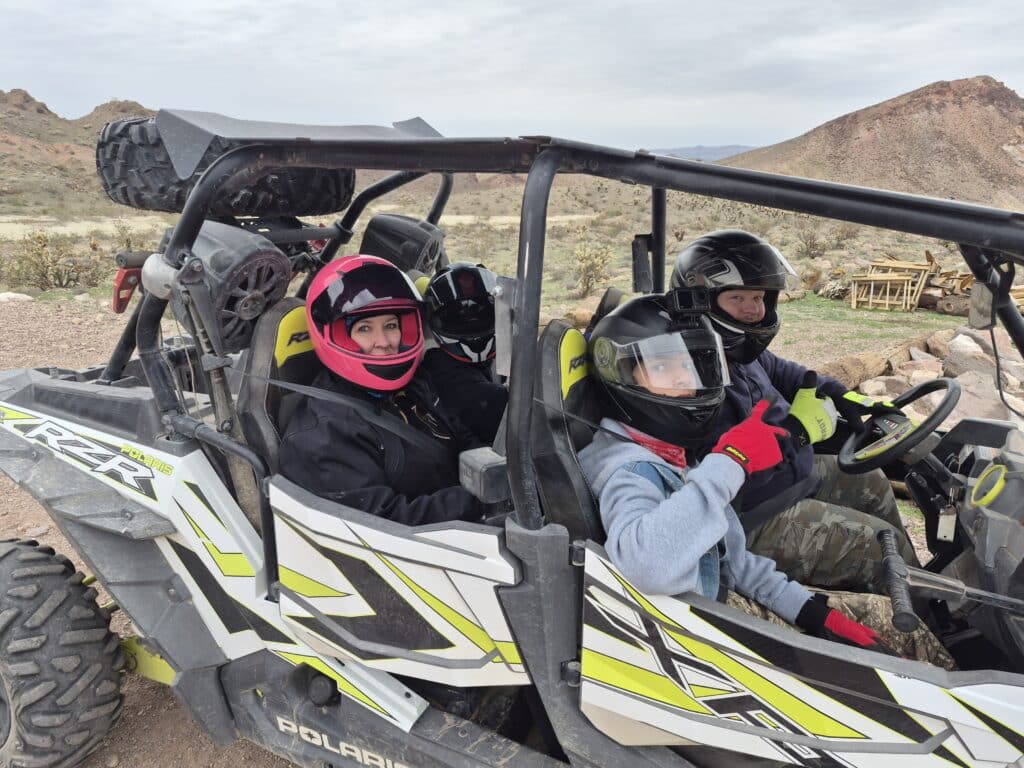 Four riders in helmets enjoy a Polaris ATV tour on a rocky Nevada trail near Las Vegas, thumbs up amid desert hills and sky.