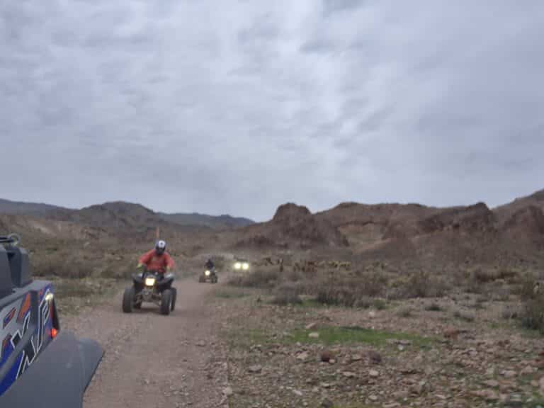 ATV riders explore a rocky desert trail near Las Vegas, Nevada, with mountains and clouds in the background on an exciting off-road tour.