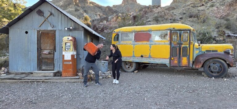 Tourists with a red gas can by vintage gas pump and old school bus at Nevada ghost town near Las Vegas desert sightseeing.