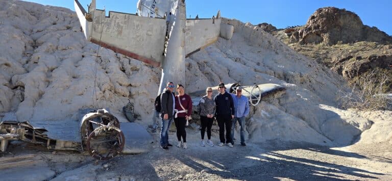Visitors pose by a crashed airplane in Nevada desert near Las Vegas, perfect for ATV tours and Ghost Town sightseeing.