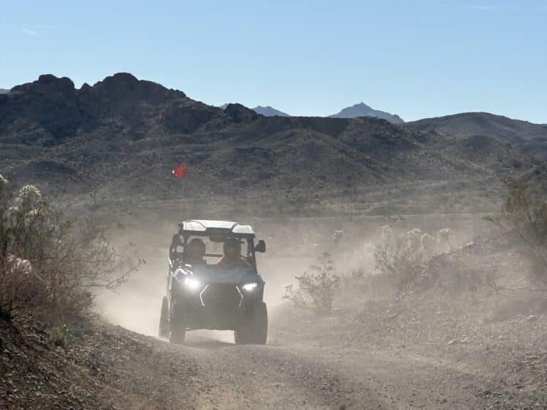 RZR off-road ride with two people on a dusty desert trail near Las Vegas, Nevada, with rocky hills and sparse vegetation.