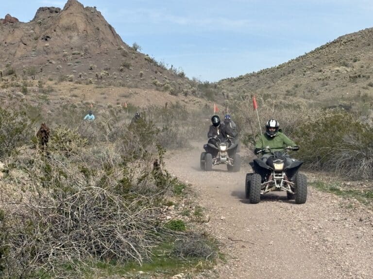 ATV riders explore a dusty Nevada desert trail near Las Vegas, with hills and shrubs under a clear sky on an exciting ATV tour.
