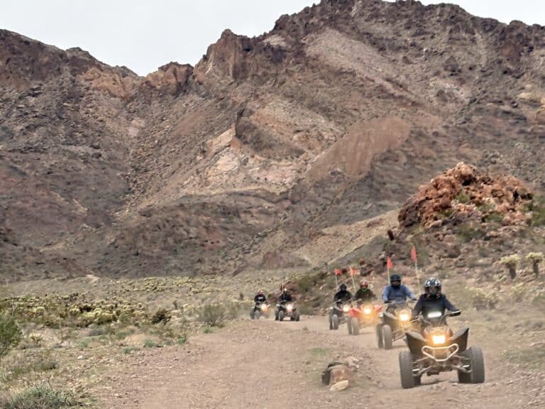 ATV riders on a Nevada desert trail near Las Vegas, heading toward mountains with orange flags, enjoy an exciting off-road tour.