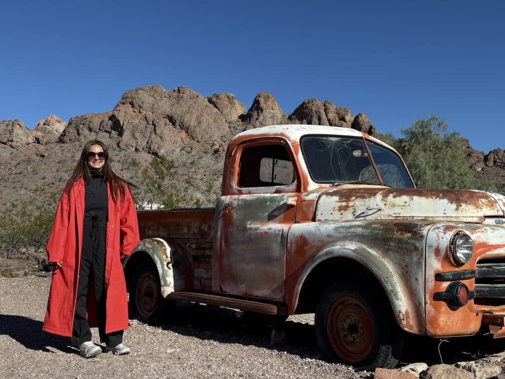 Woman in red coat by vintage pickup near Nevada desert hills, perfect for Ghost Town sightseeing or Las Vegas ATV tours.