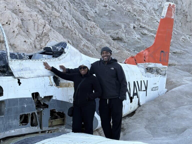 Smiling duo by a wrecked Navy plane in Nevada desert near Las Vegas, ideal for ATV tours and ghost town sightseeing.