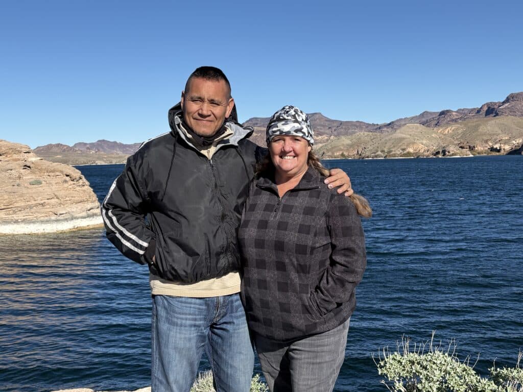 Couple smiling by Colorado River near Las Vegas, Nevada, with rocky mountains—dressed warmly for off-road ATV adventures.