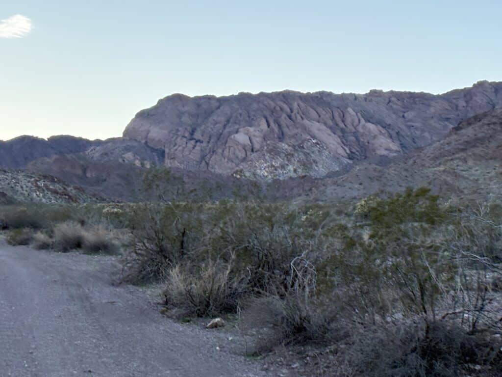 Nevada dirt road with desert shrubs leads to rocky mountains near Las Vegas, perfect for RZR rides or Ghost Town tours at dusk.