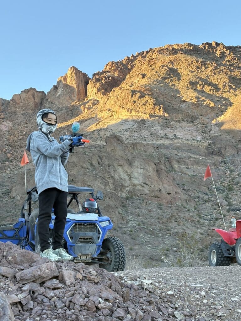 A person in a gray hoodie with a camera stands near ATVs, ready for an ATV tour on Nevada’s rugged terrain near Las Vegas.