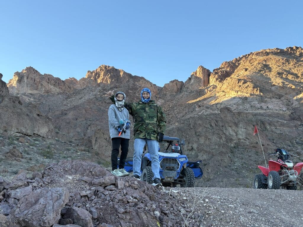 Adventurers in helmets pose by ATVs on rocky Nevada terrain near Las Vegas with mountains, perfect for ATV tours and RZR off-road rides.