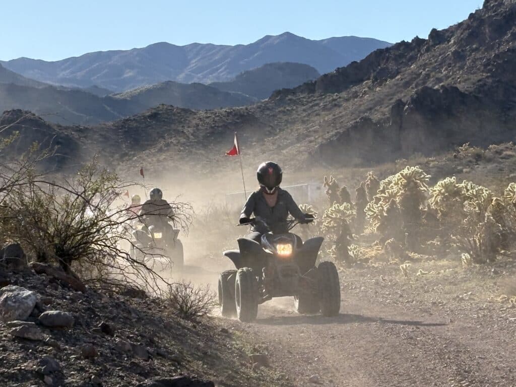ATV riders explore a dusty Nevada desert trail near Las Vegas with cacti, mountains, and Colorado River views.