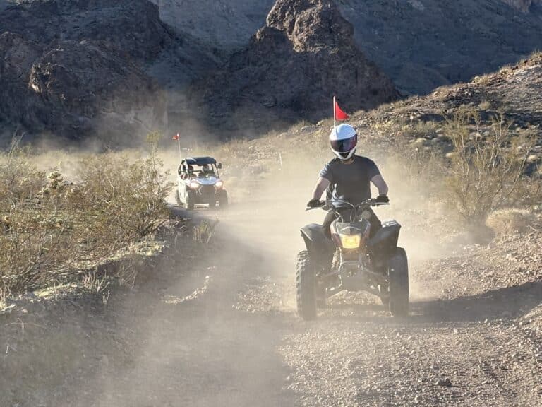 Helmeted rider leads an ATV on a dusty Nevada trail near Las Vegas, surrounded by rocky hills; perfect for ATV tours.