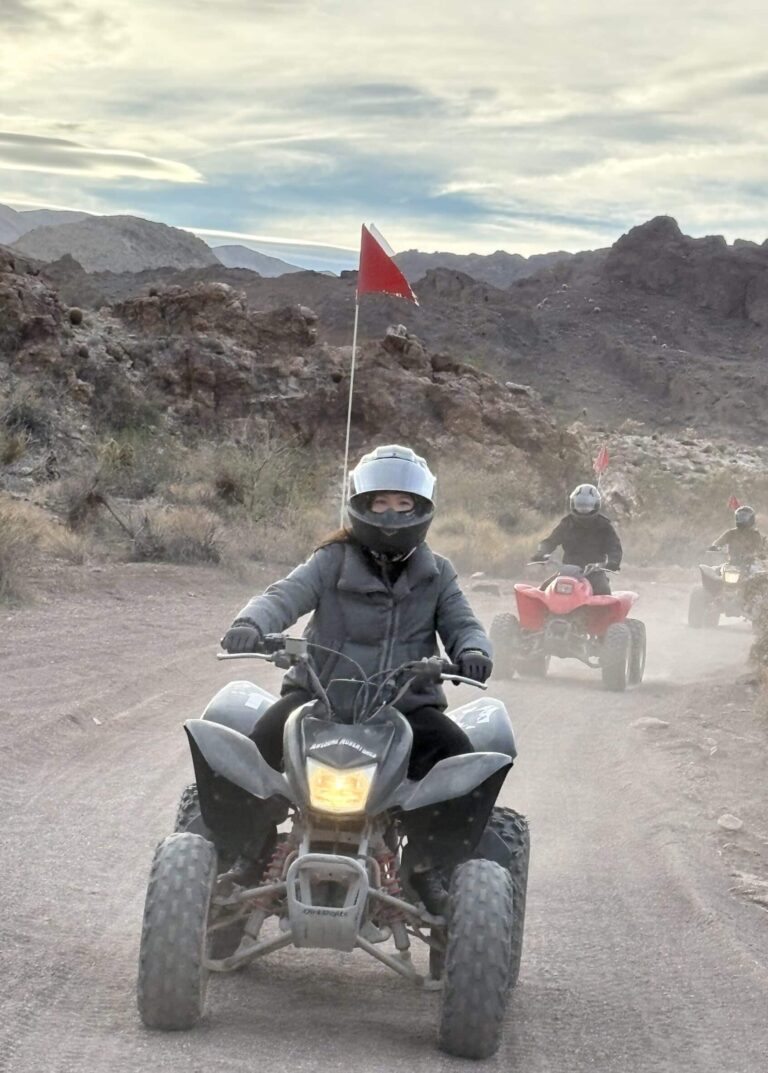 ATV riders in Nevada near Las Vegas explore dusty desert trails with red flags, rocky hills, and cloudy skies on an off-road tour.
