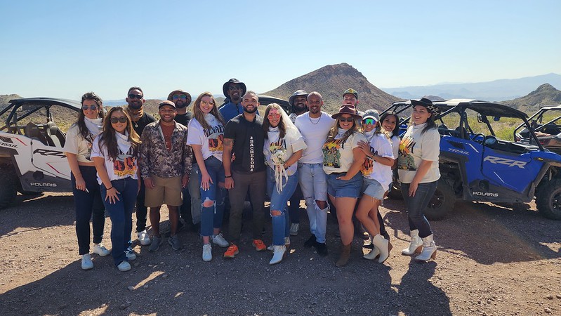 Group enjoys Las Vegas RZR ATV tour in Nevada, posing by off-road vehicles with mountains and blue sky near Colorado River.